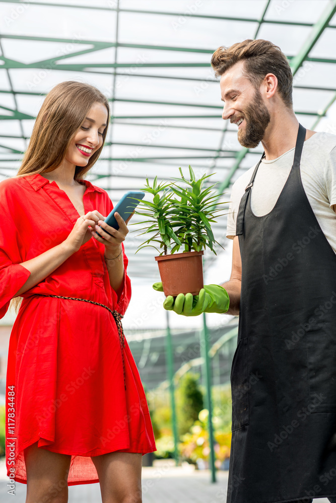 英俊的卖花人站在植物店里帮助女买家选花。女人是我们