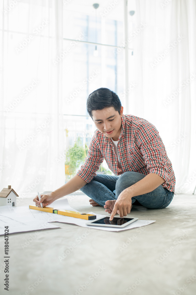 Young handsome male asian architect working at home on the floor