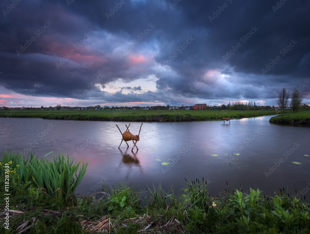 Beautiful dramatic sky with colorful clouds with water channel at sunset in Kinderdijk, Netherlands.