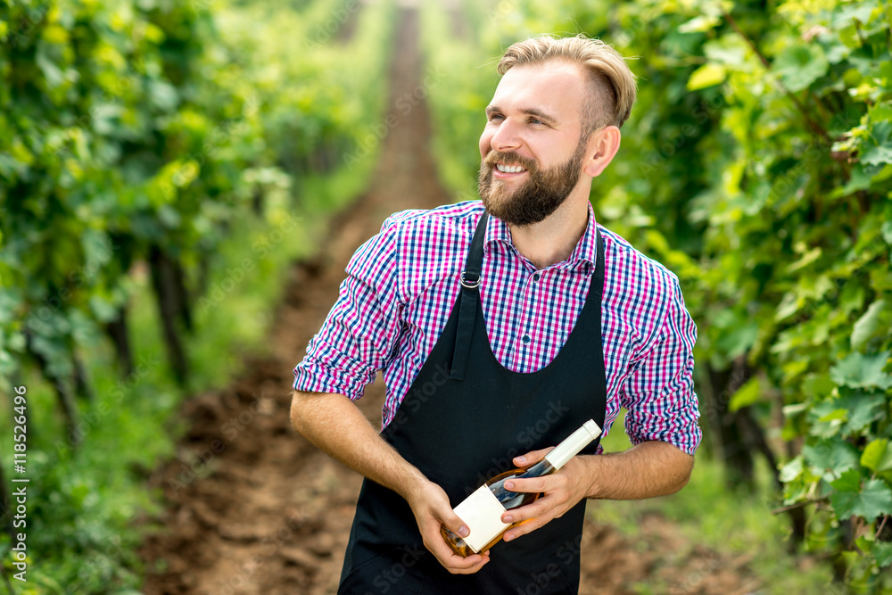 Portrait of handsome wine maker in apron with bottle of white wine standing on the vineyard