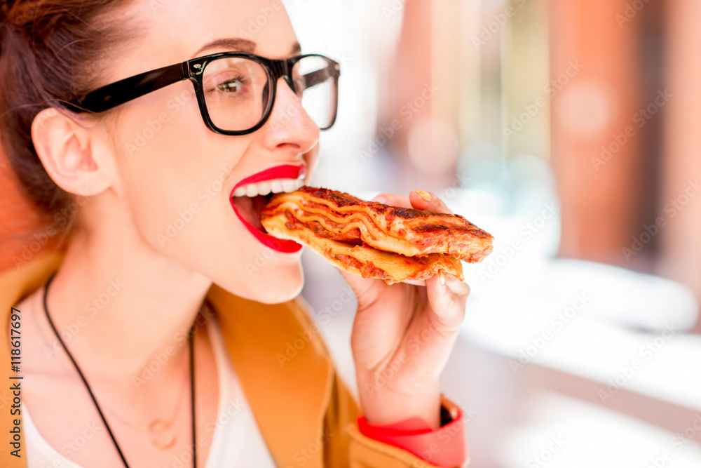 Young woman eating lasagna with bolognese outdoors on the street in Bologna city in Italy. Lasagna b