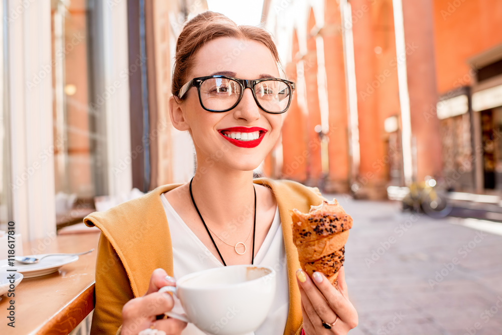 Young woman having italian breakfast with croissant and coffee at the cafe on the street in Bologna 