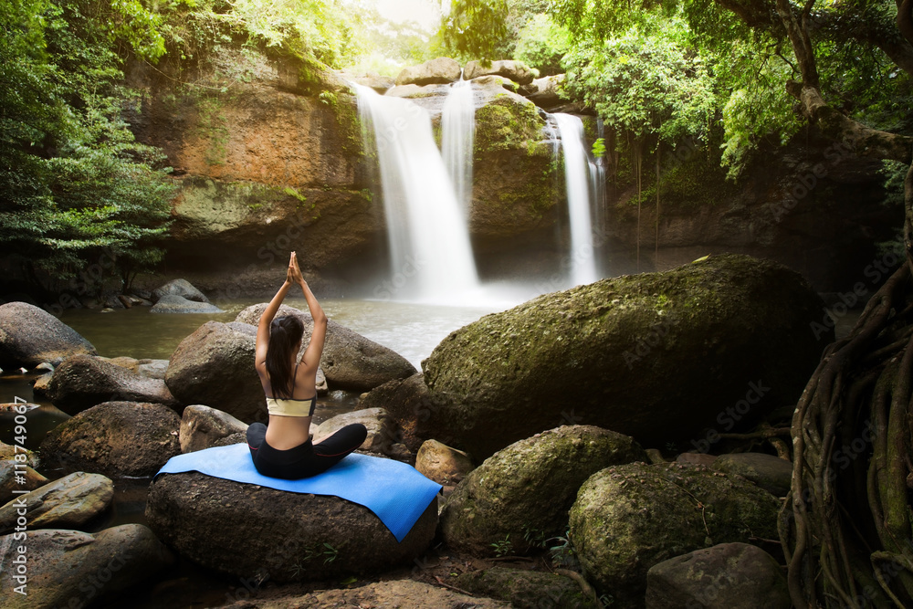 Young woman in a yoga pose at the waterfall, she felt relaxed. T