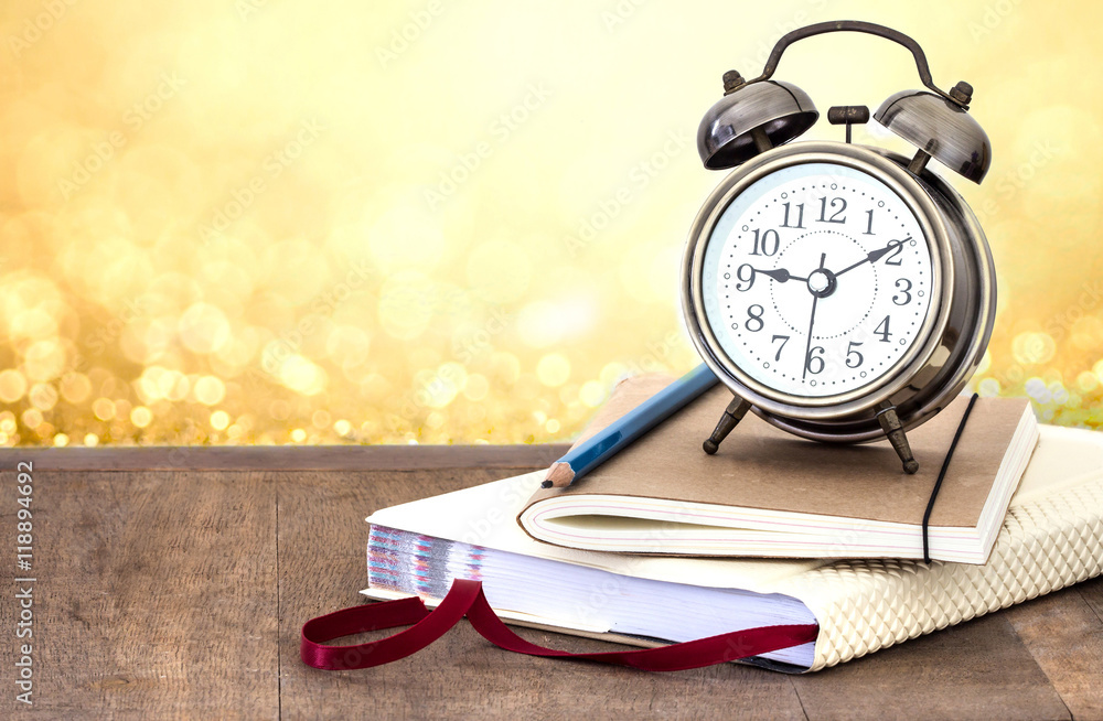 a vintage alarm clock  and books on wooden table with glowing go