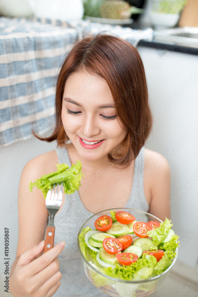 美丽的年轻亚洲女孩在吃沙拉。微笑的快乐女孩在吃