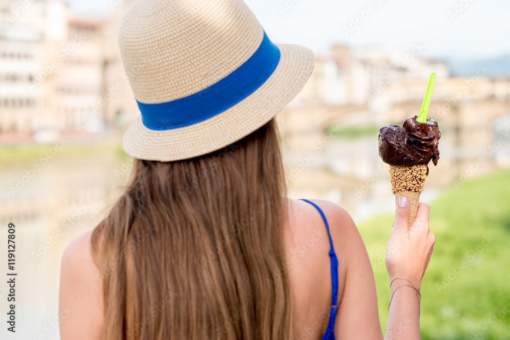 坐在河边，穿着蓝色连衣裙的年轻女游客拿着华夫饼筒里的巧克力冰淇淋