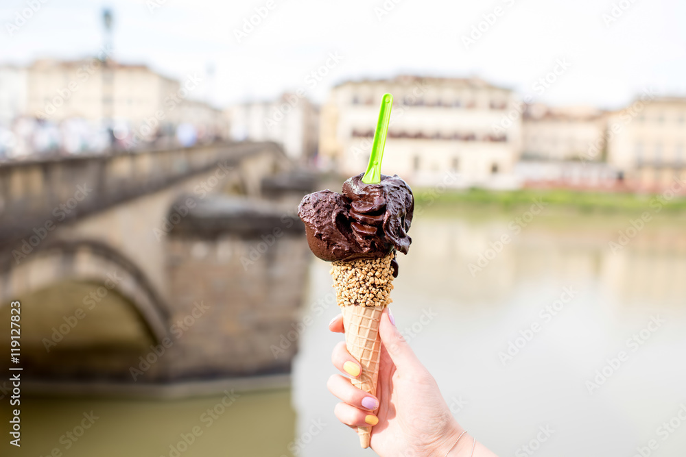 Female hand holding chocolate ice cream in waffle cone on Florence city background. Italian traditio