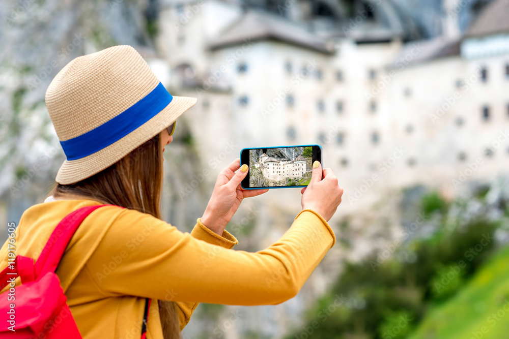 年轻的女旅行者用手机拍摄Predjama城堡。这座城堡是著名的旅游景点