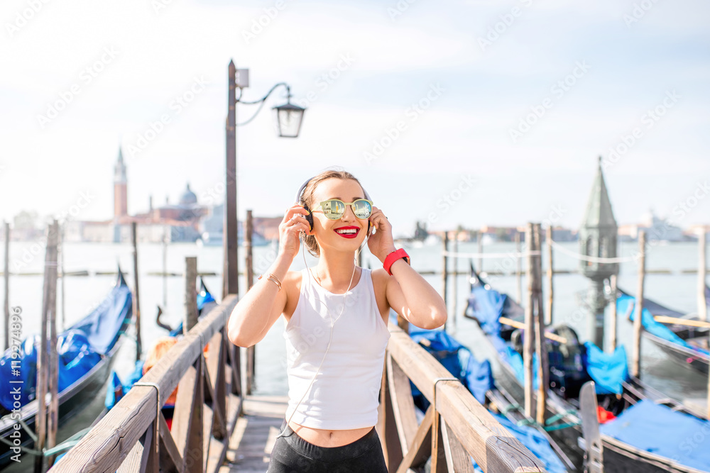 Young woman in sportswear listening to the music on the pier in Venice. Morning exercise in the old 