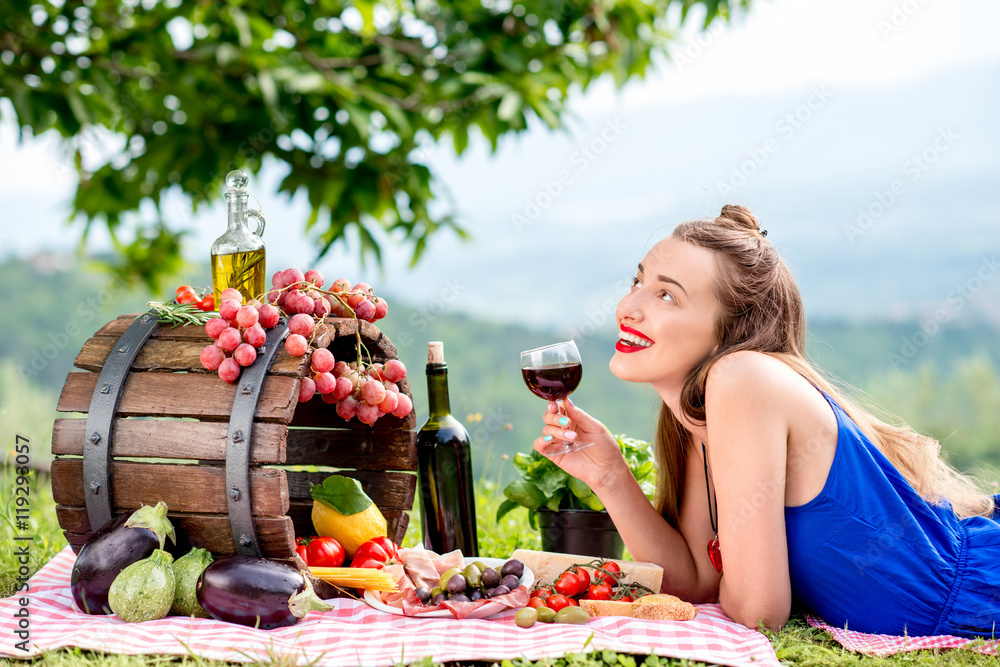 美丽的女人躺在草地上，手里拿着很多美味的意大利食物和葡萄酒，在土族的乡村