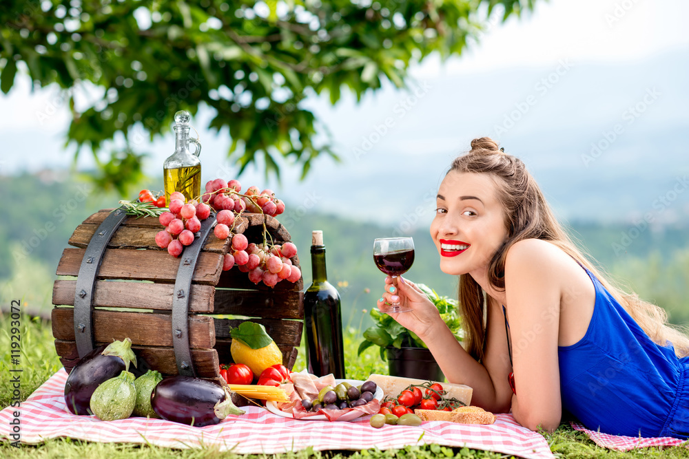 Beautiful woman lying on the grass with lots of tasty italian food and wine in the countryside in Tu