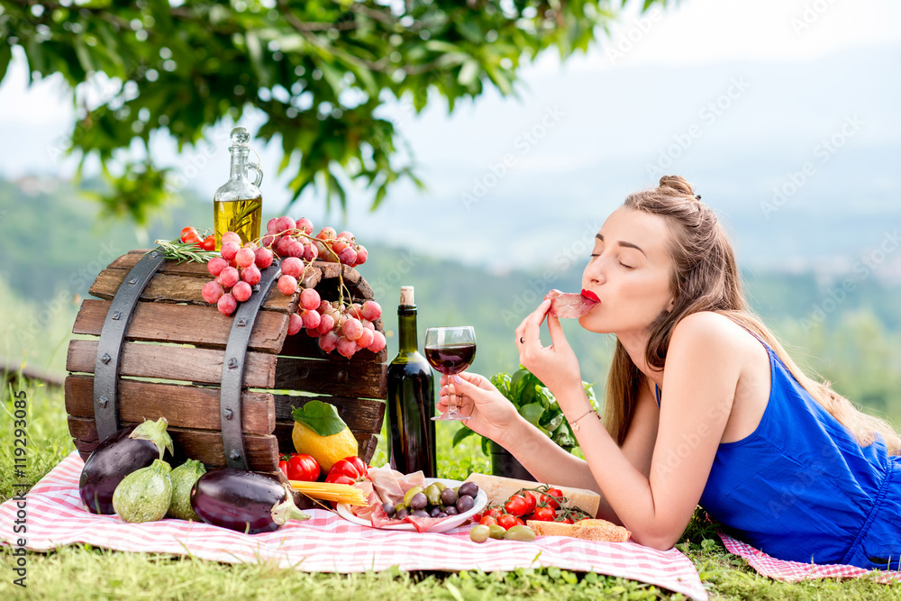 美丽的女人躺在草地上品尝火腿，里面有很多美味的意大利食物和葡萄酒