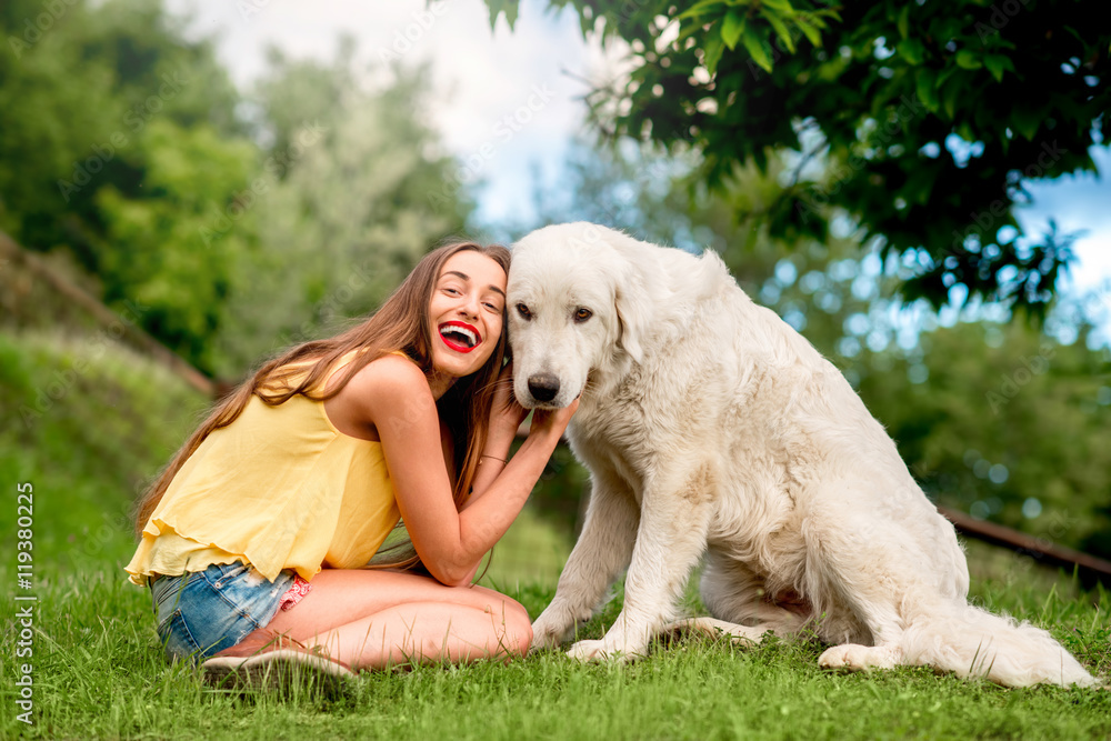 年轻快乐的女人在托斯卡纳乡村的草坪上与Maremma意大利牧羊犬玩耍