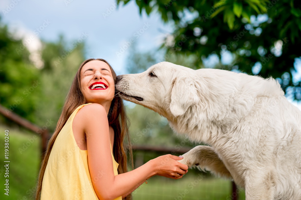 年轻快乐的女人在托斯卡纳乡村的草坪上与Maremma意大利牧羊犬玩耍