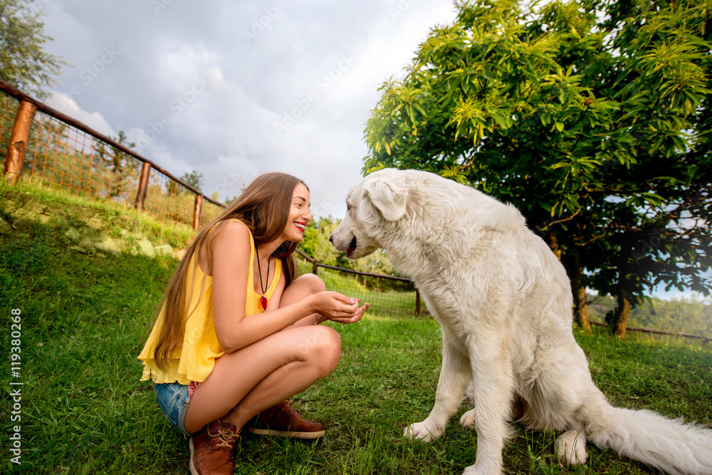 年轻快乐的女人在托斯卡纳乡村的草坪上与Maremma意大利牧羊犬玩耍