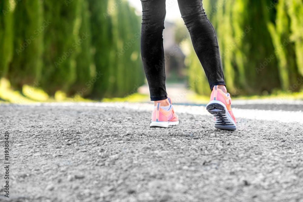 Female legs in sport sneakers in start position on the gravel road