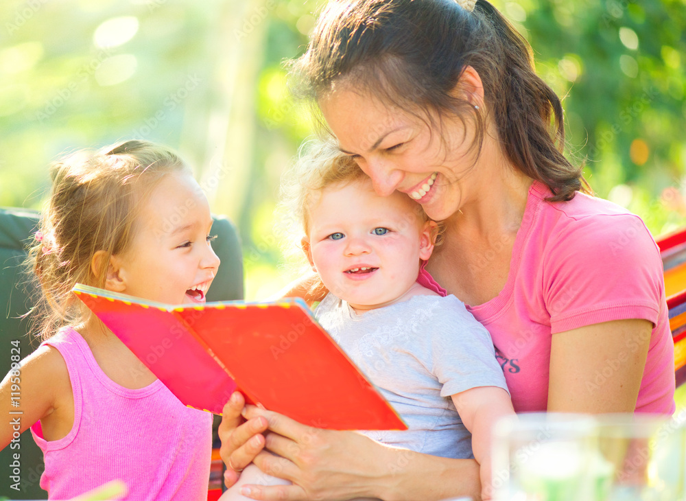 Happy mother reading a book to her children in sunny park