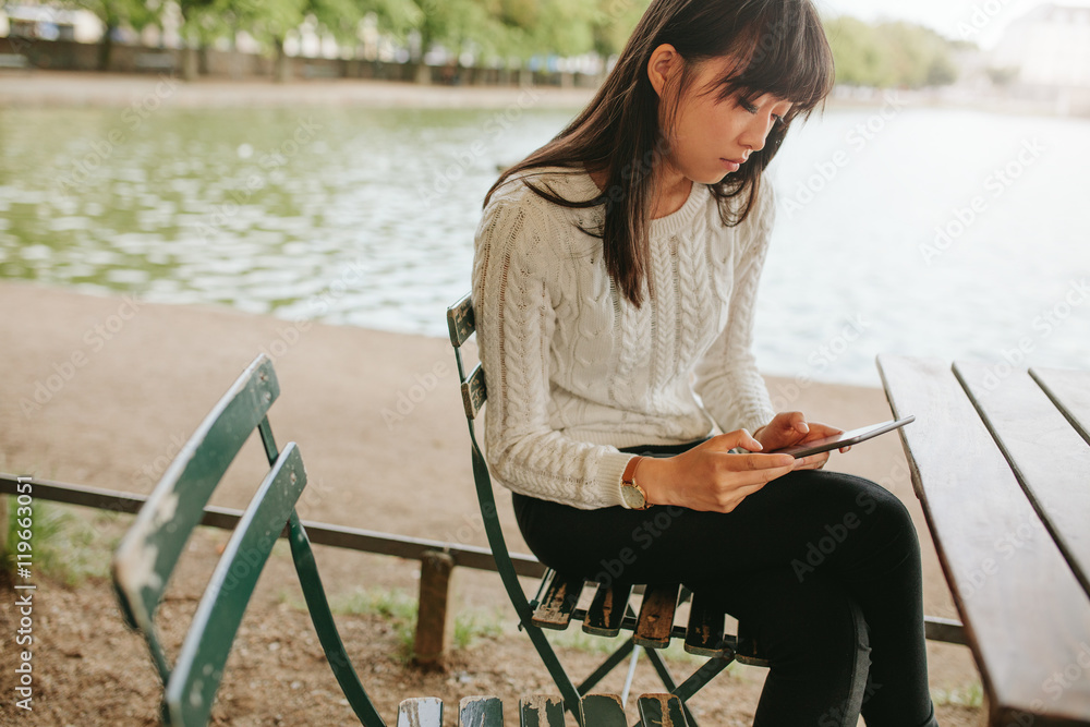 Woman at cafe by the pond using digital tablet