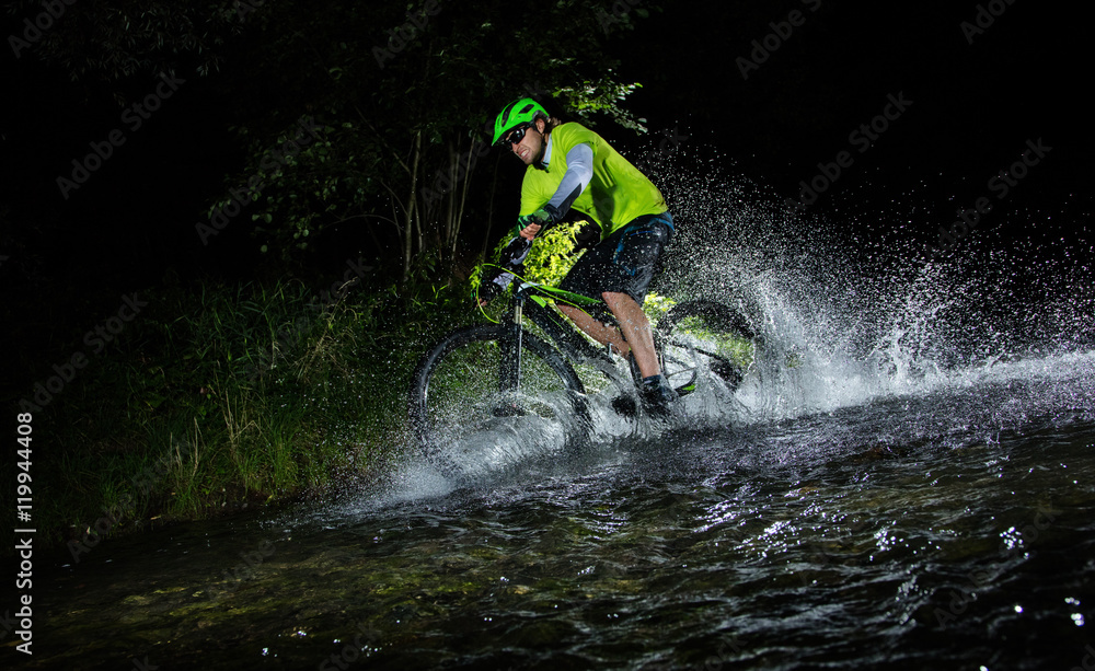 Mountain biker splashing in forest stream at night