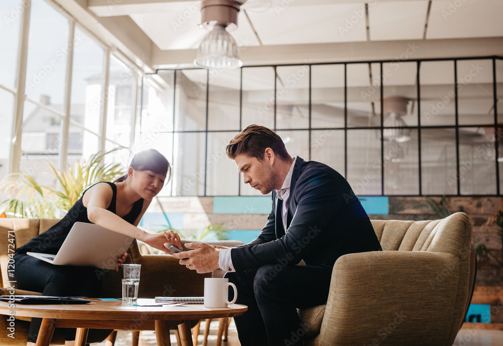 Two people sitting in office lobby using mobile phone