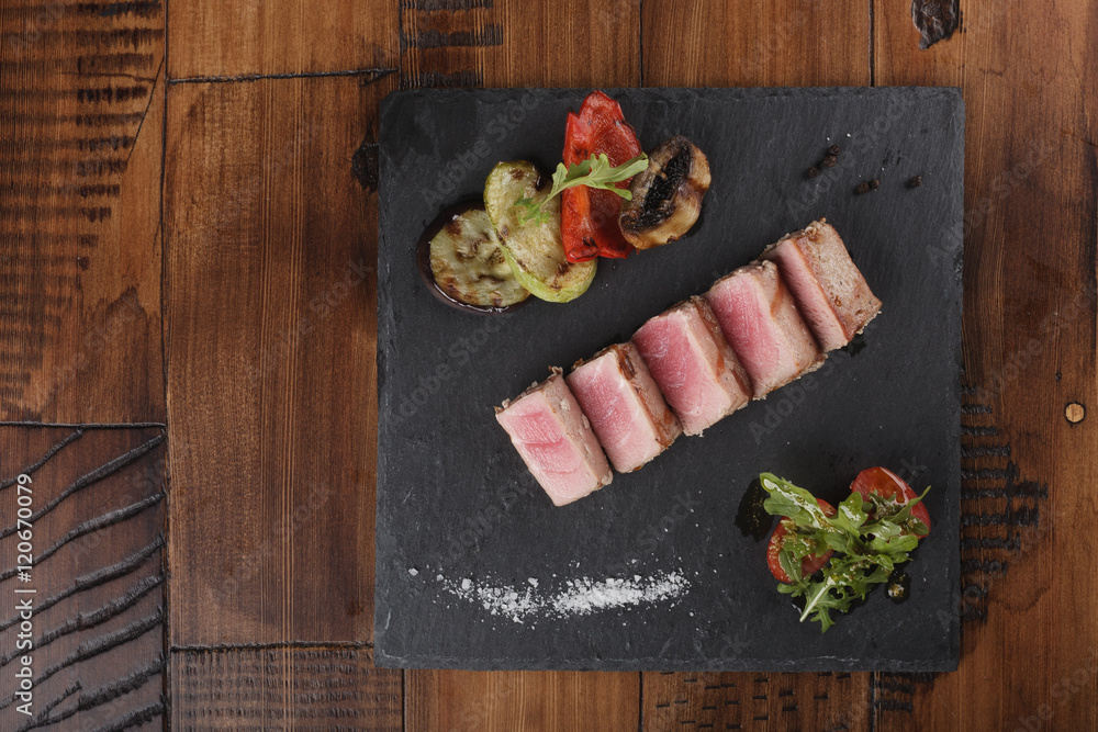 Tuna fillet slices with salad on a slate. Wooden background