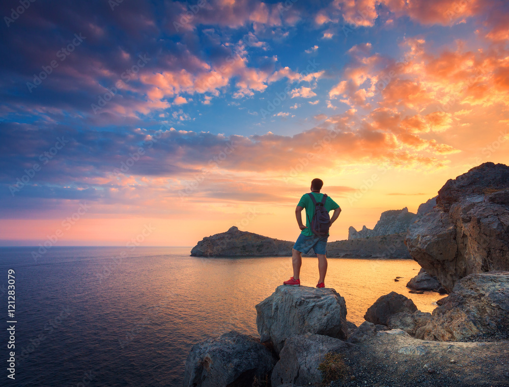 Beautiful summer landscape with standing man with backpack on the stone at the ocean against the col