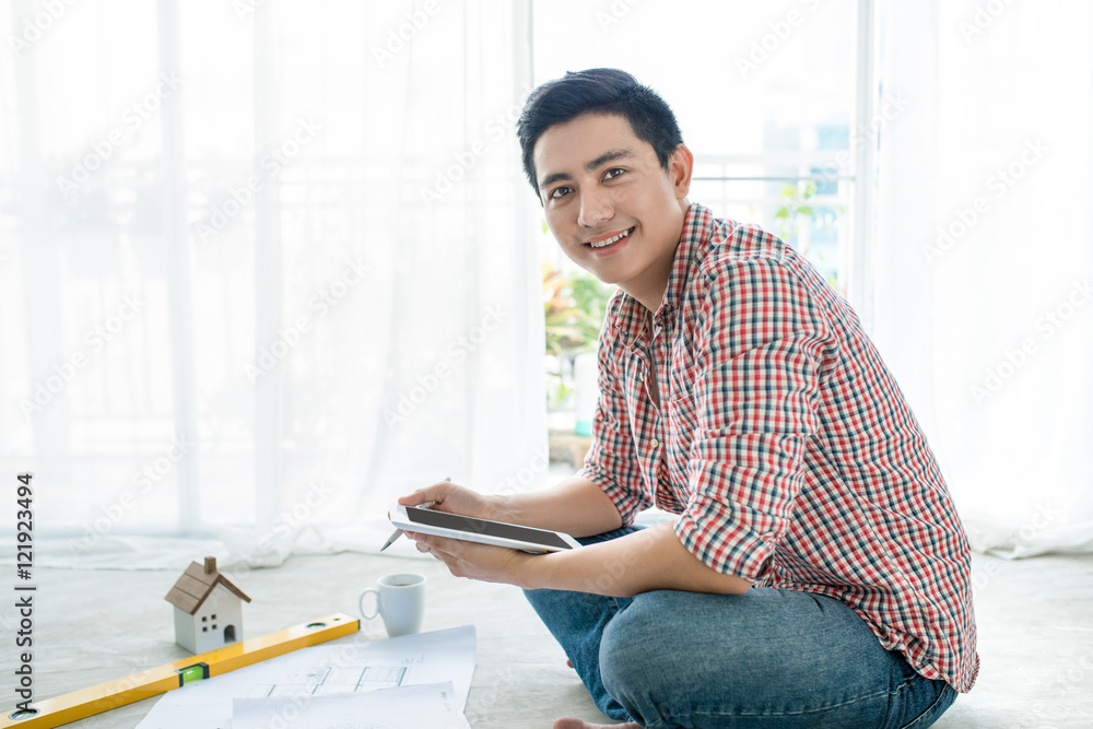 Young handsome male asian architect working at home using tablet on the floor.