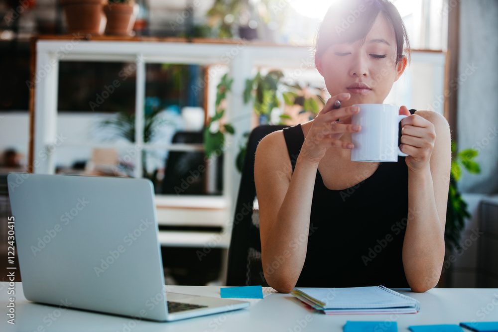 放松的年轻女人在办公桌前喝咖啡