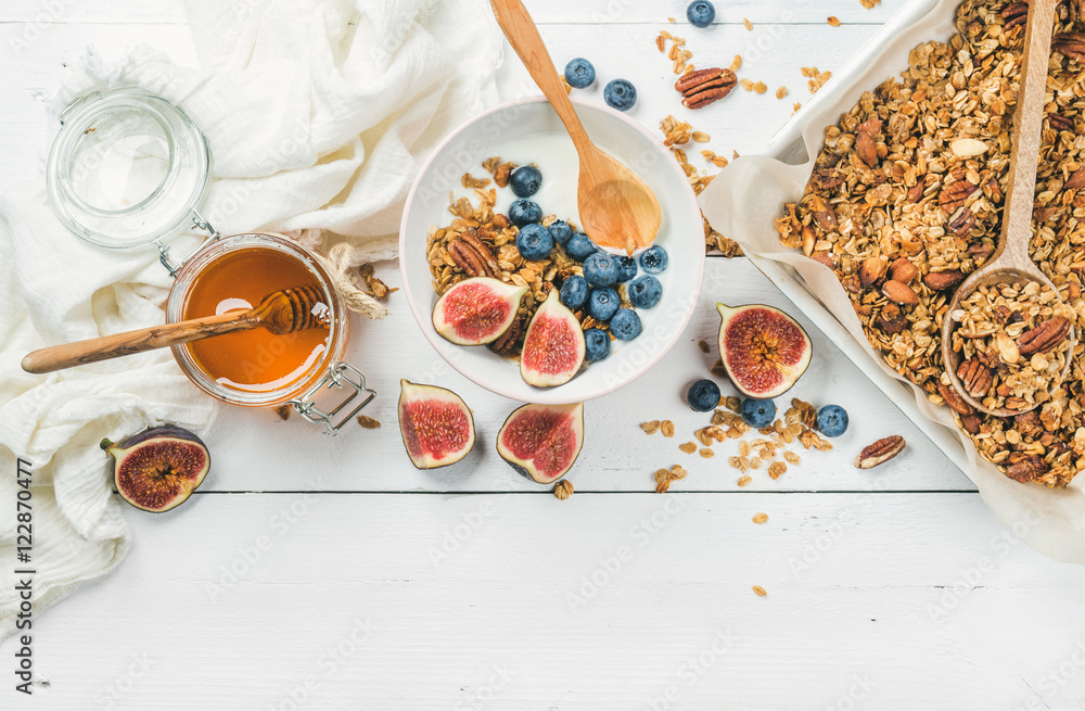 Healthy breakfast set. Oat granola with nuts, yogurt, honey, fresh figs and blueberries in bowl on w