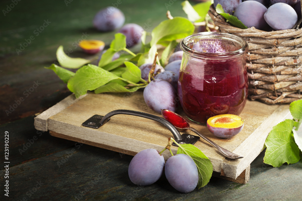 Plums and jar of jam on table