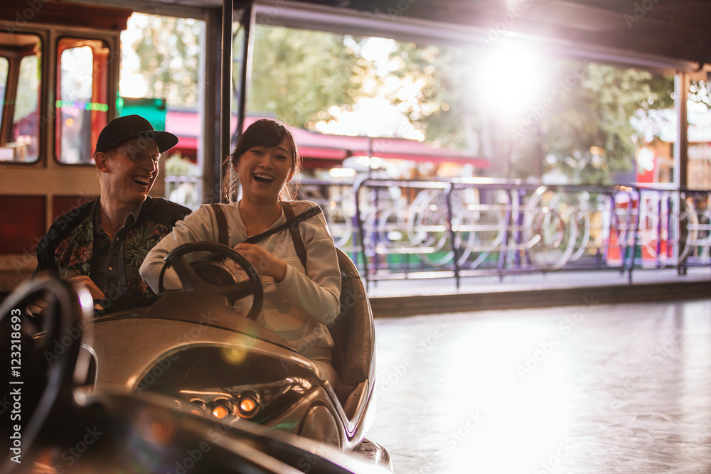 Young man and woman driving bumper car at fairground