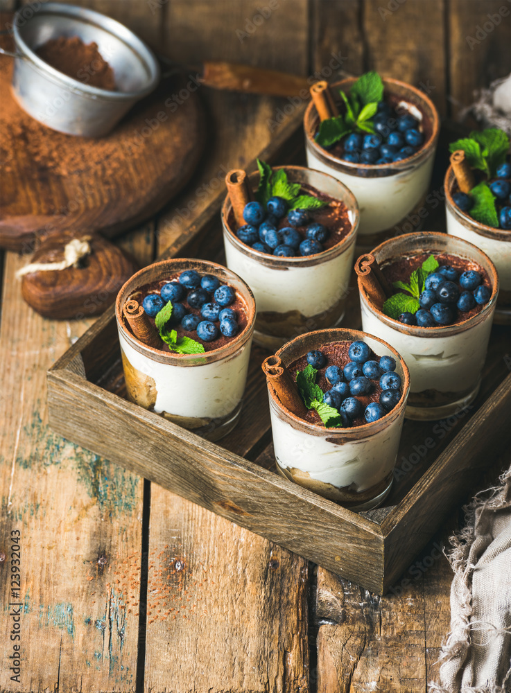 Homemade Tiramisu dessert in glasses with cinnamon, mint and fresh garden blueberris in wooden tray 