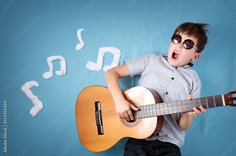 happy seven years old boy on blue blanket background with acoustic guitar and musical notes. Young g