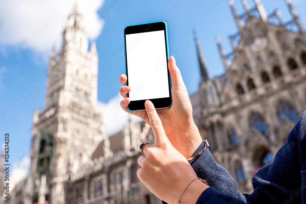 Holding a smart phone with white screen on the central city square background in Munich, Germany