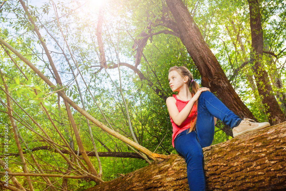 Beautiful teenage girl sitting on fallen tree