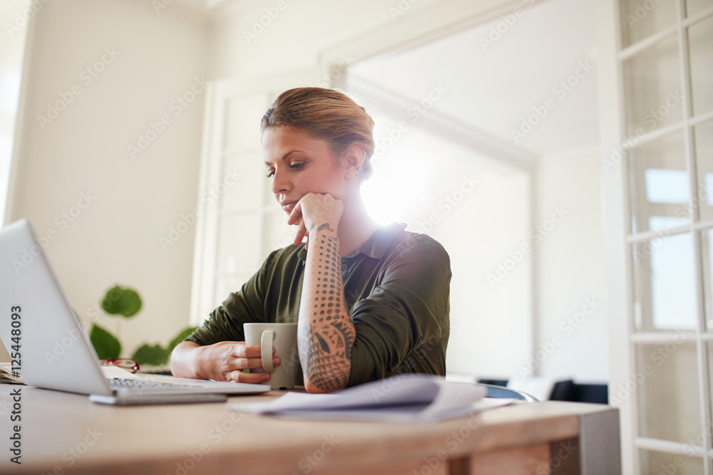 Young woman with coffee looking at laptop