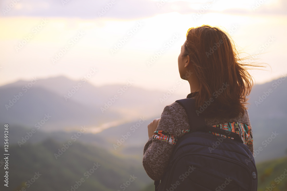 Hipster young woman with backpack enjoying sunrise view on mountain