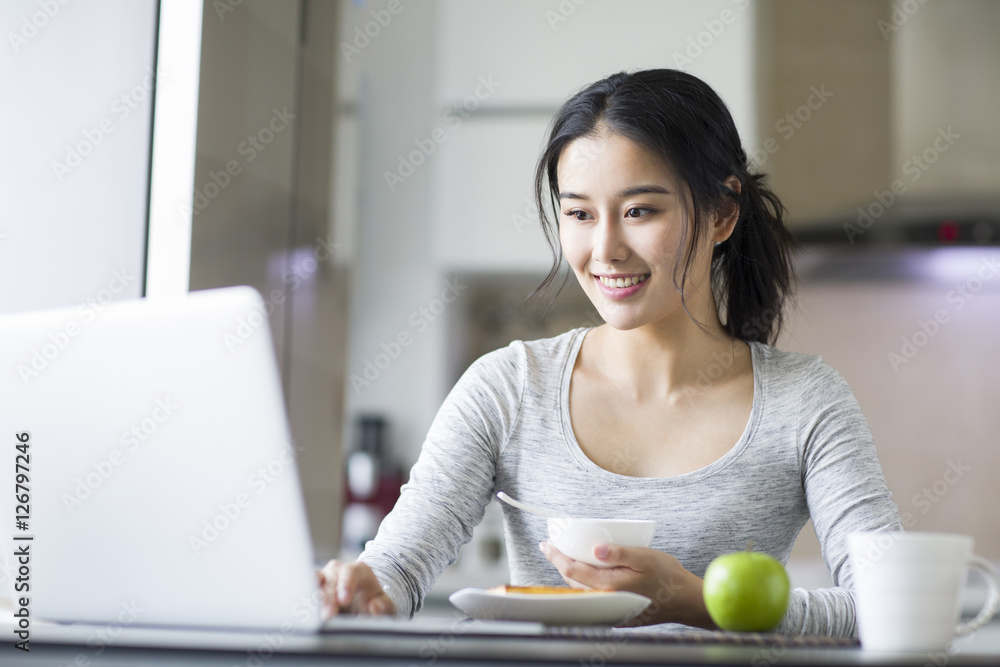 年轻女子早餐时使用笔记本电脑