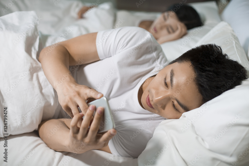 Young husband using smart phone on bed