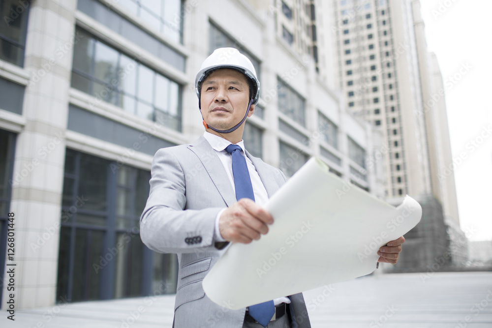 Male architect looking at view with blueprint outdoors