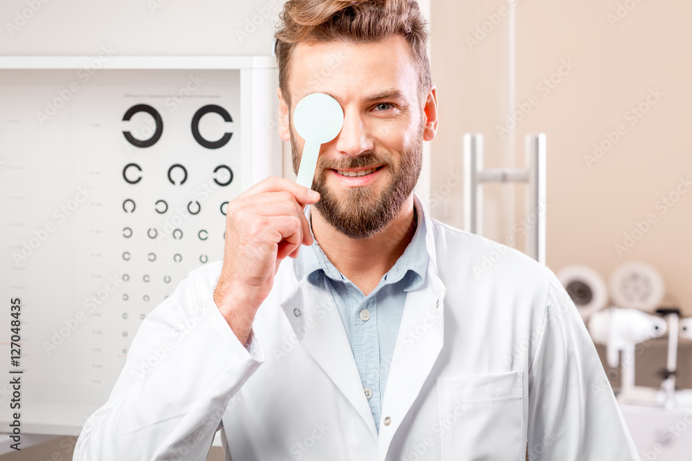 Portrait of handsome ophthalmologist in front of the eye chart in the cabinet