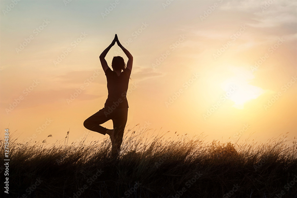 silhouette of woman practicing yoga on the nature at sunset background