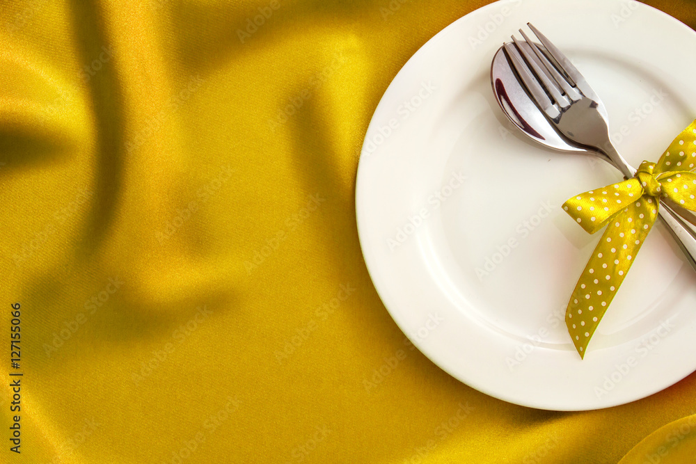  White empty plate with fork and spoon on gold silk fabric 