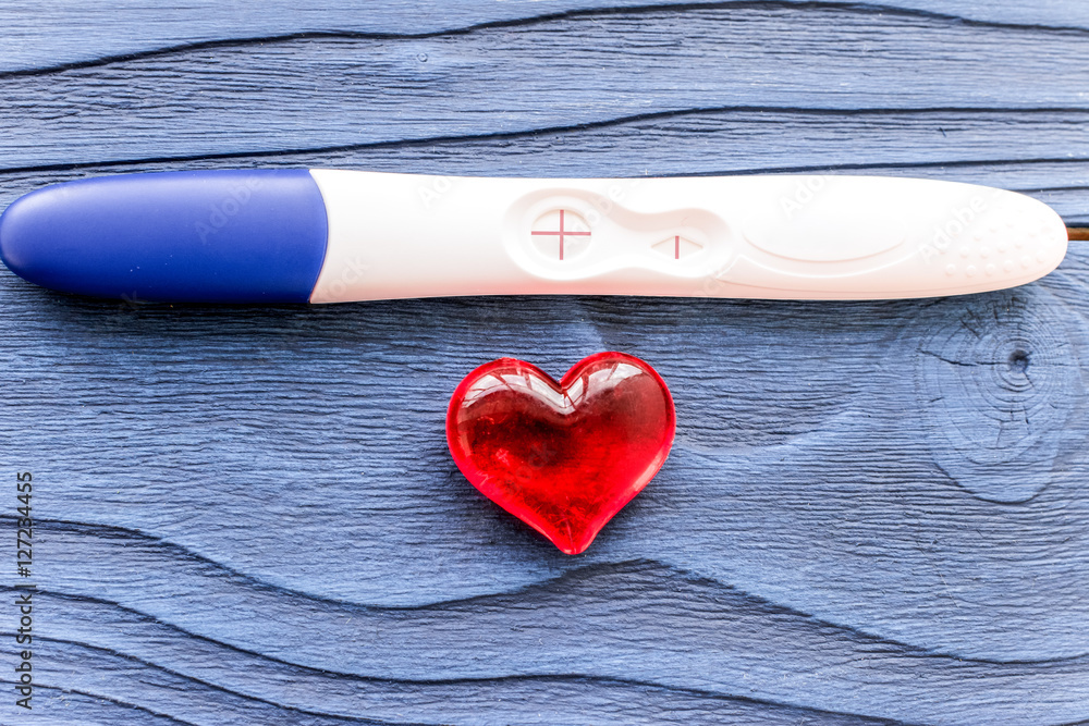 Positive pregnancy test with heart on wooden background top view