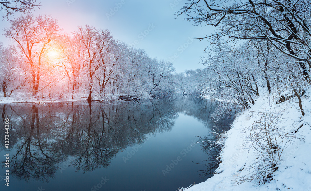 日落时河上的冬季森林。白雪皑皑的树木、阳光、美丽的冰冻ri的全景景观