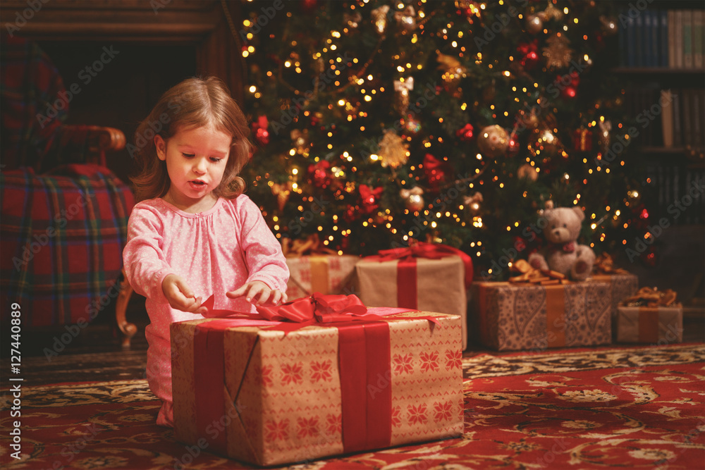 child girl in a nightgown in Christmas night opening gifts at Ch