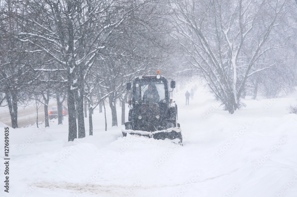 Snow machine tractor cleans snow on street in winter in heavy snow. Passers-by people on the street 