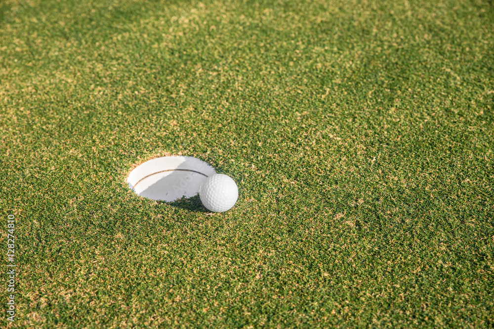 Golf ball sits at the lip of the hole on the putting green.