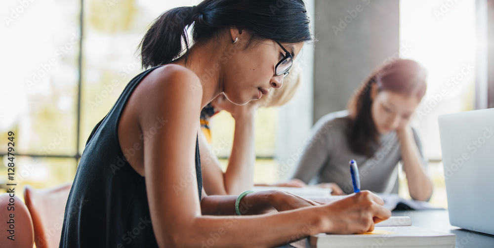 Woman writing with classmates studying in library