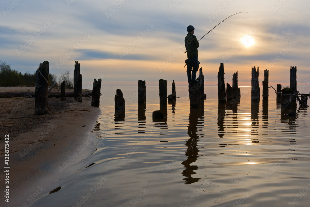 Silhouette of boy on pole of pier catching fish.